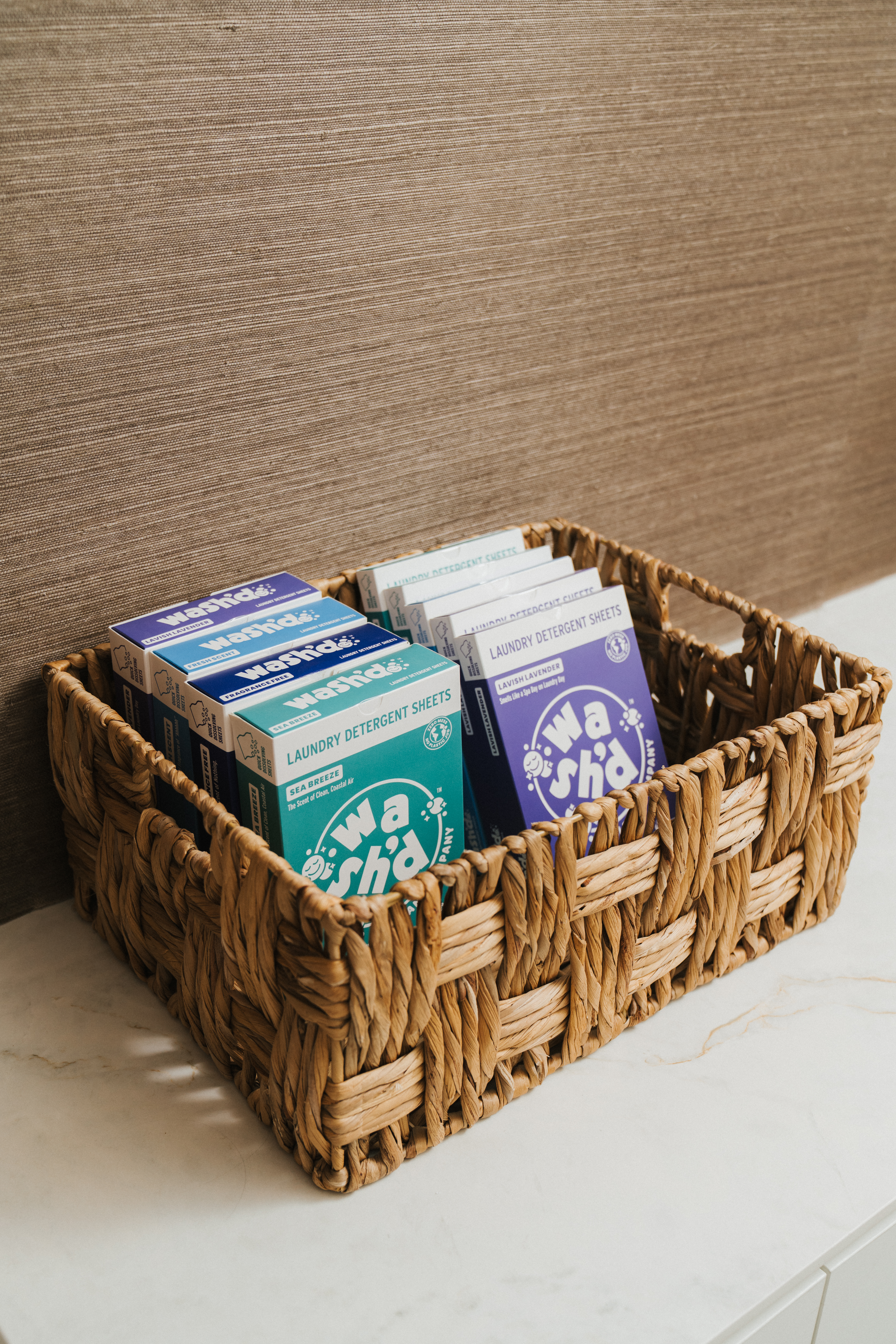 A basket holding multiple boxes of Wash'd blue and teal packaging on a white surface